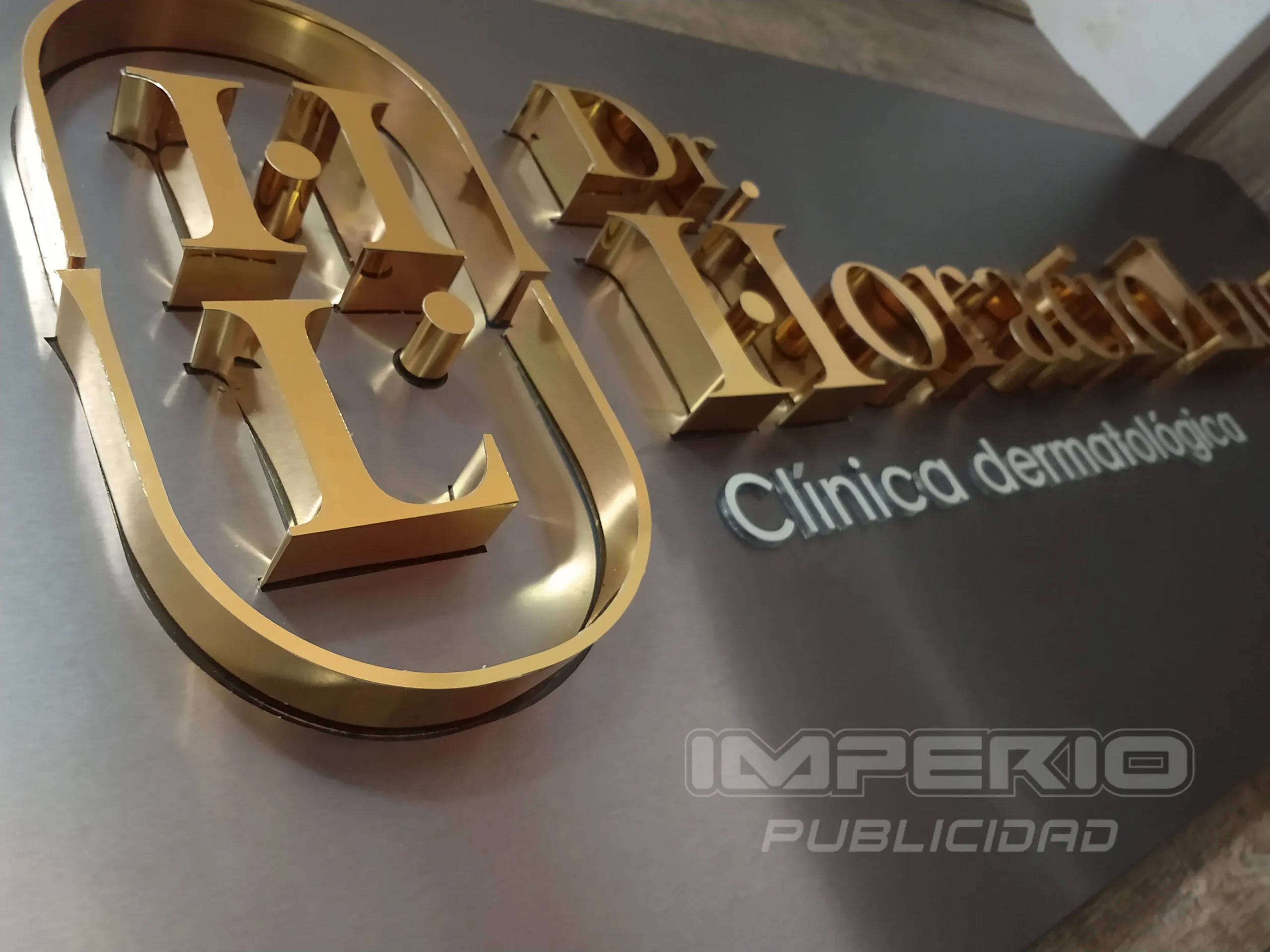 Letrero 3D dorado con letras corpóreas en acero inoxidable montado sobre base de acero cepillado, fabricado por Imperio Publicidad CDMX.