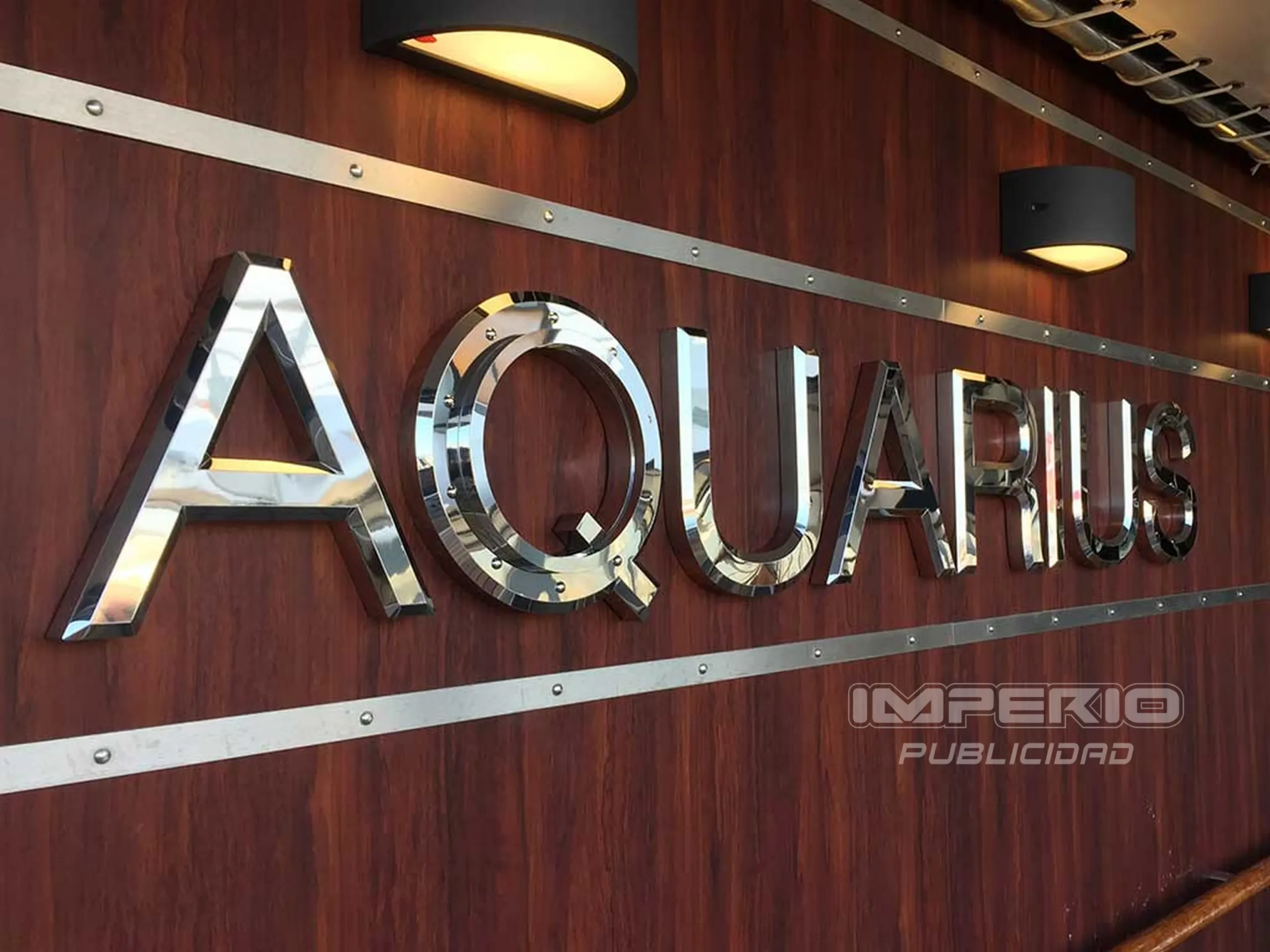 Letras 3D de acero inoxidable cromado montadas en pared de madera para recepción corporativa en CDMX