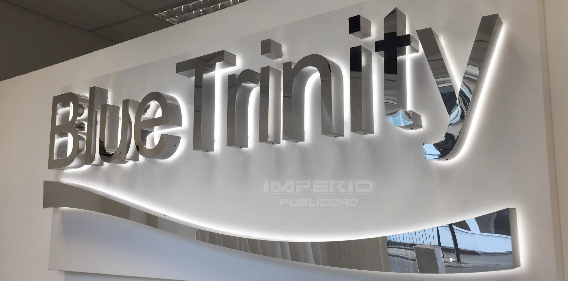 Letrero corporativo con letras 3D de acero inoxidable espejo retroiluminadas con halo LED en pared interior