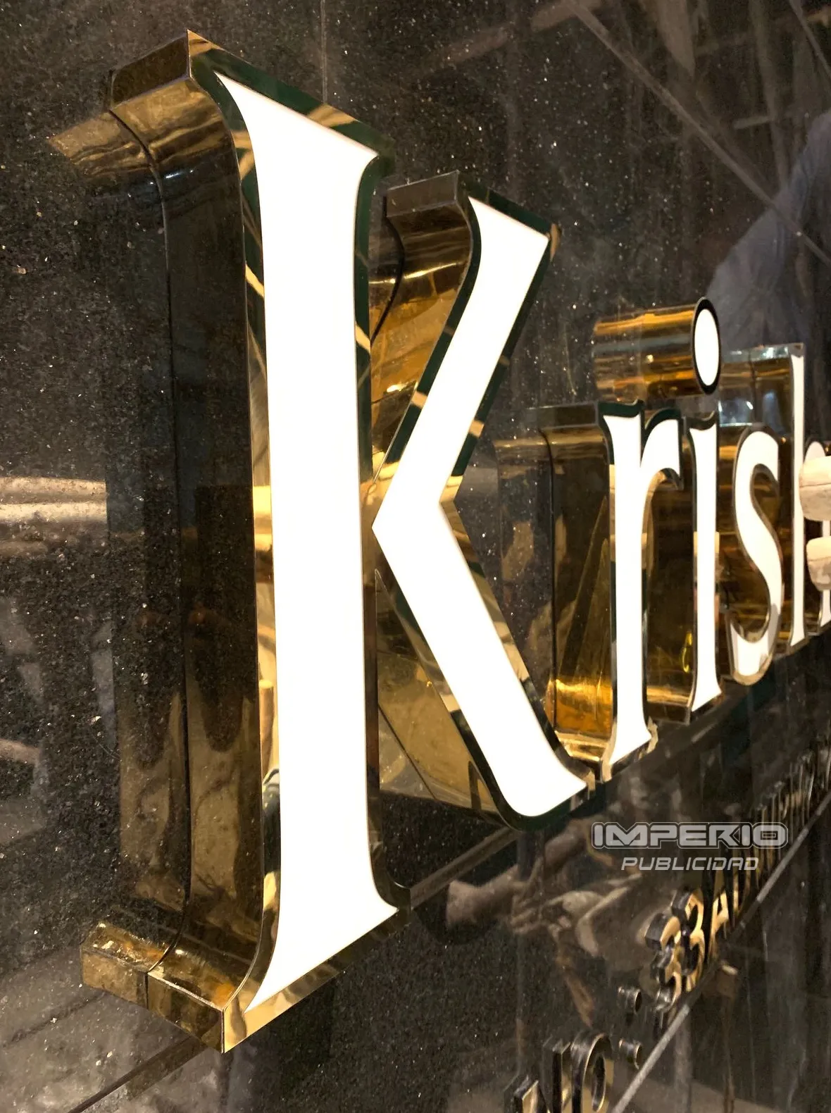 Logotipo 3D de aluminio dorado espejo con frente acrílico iluminado con LED en recepción corporativa en CDMX