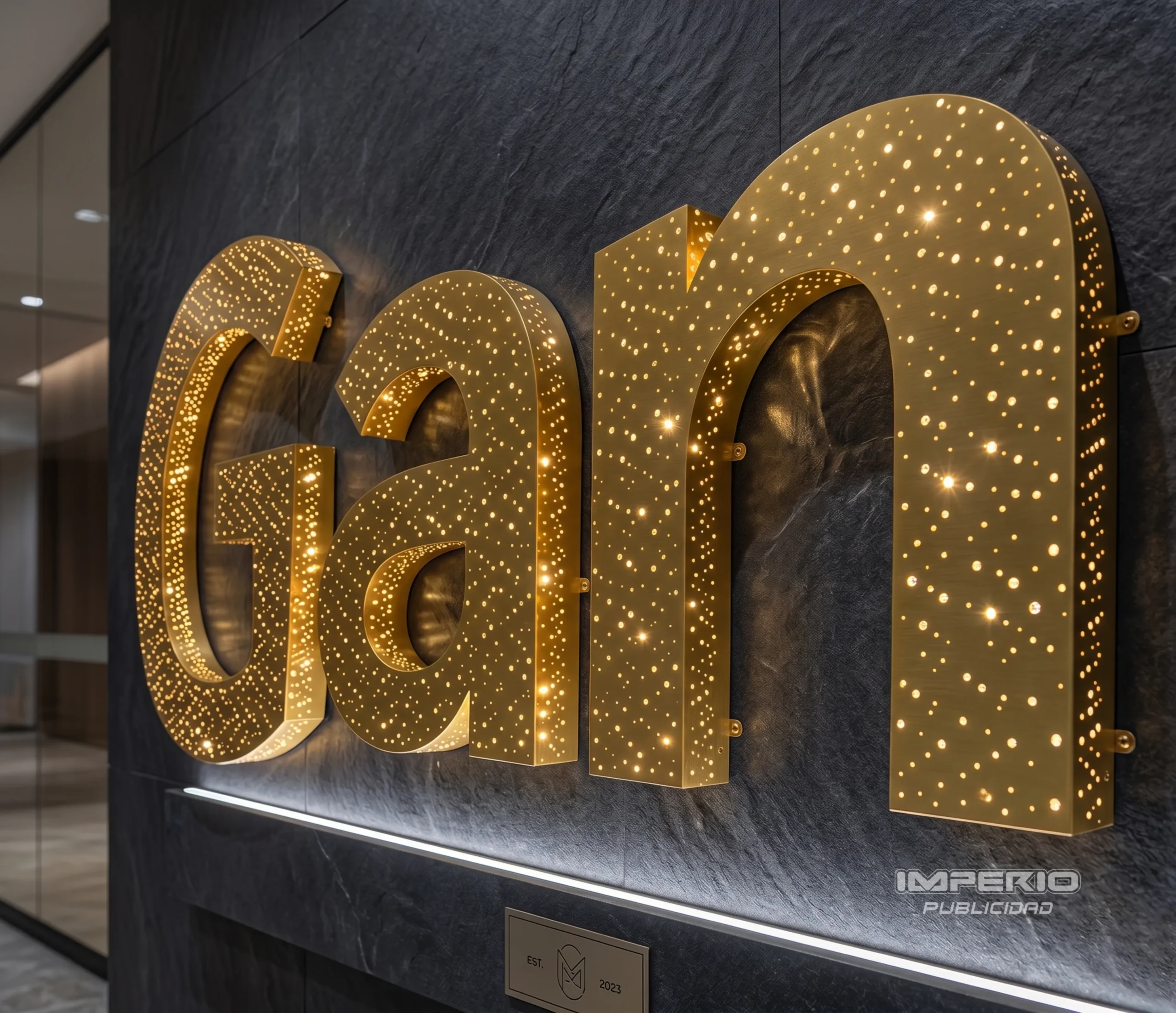 Letras 3D perforadas tipo galaxia con iluminación LED cálida en acero dorado para interiores corporativos en CDMX